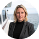 Angela Murray with shoulder-length blonde hair in a dark blazer and black top stands on a boat deck with water and sky in the background.